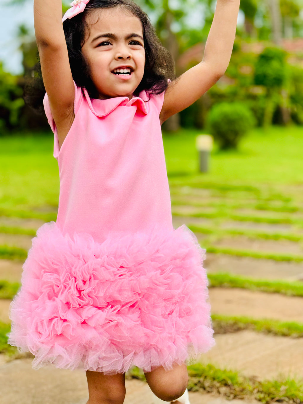 Young girl in a pink dress with a ruffled skirt outdoors on a sunny day.
