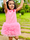 Young girl in a pink dress with a ruffled skirt outdoors on a sunny day.