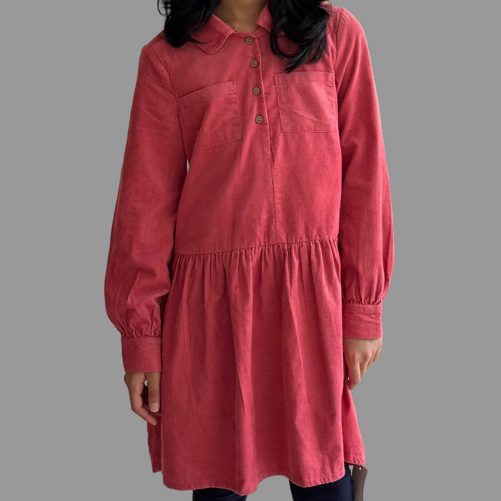 Young girl wearing a pink dress against a plain wall