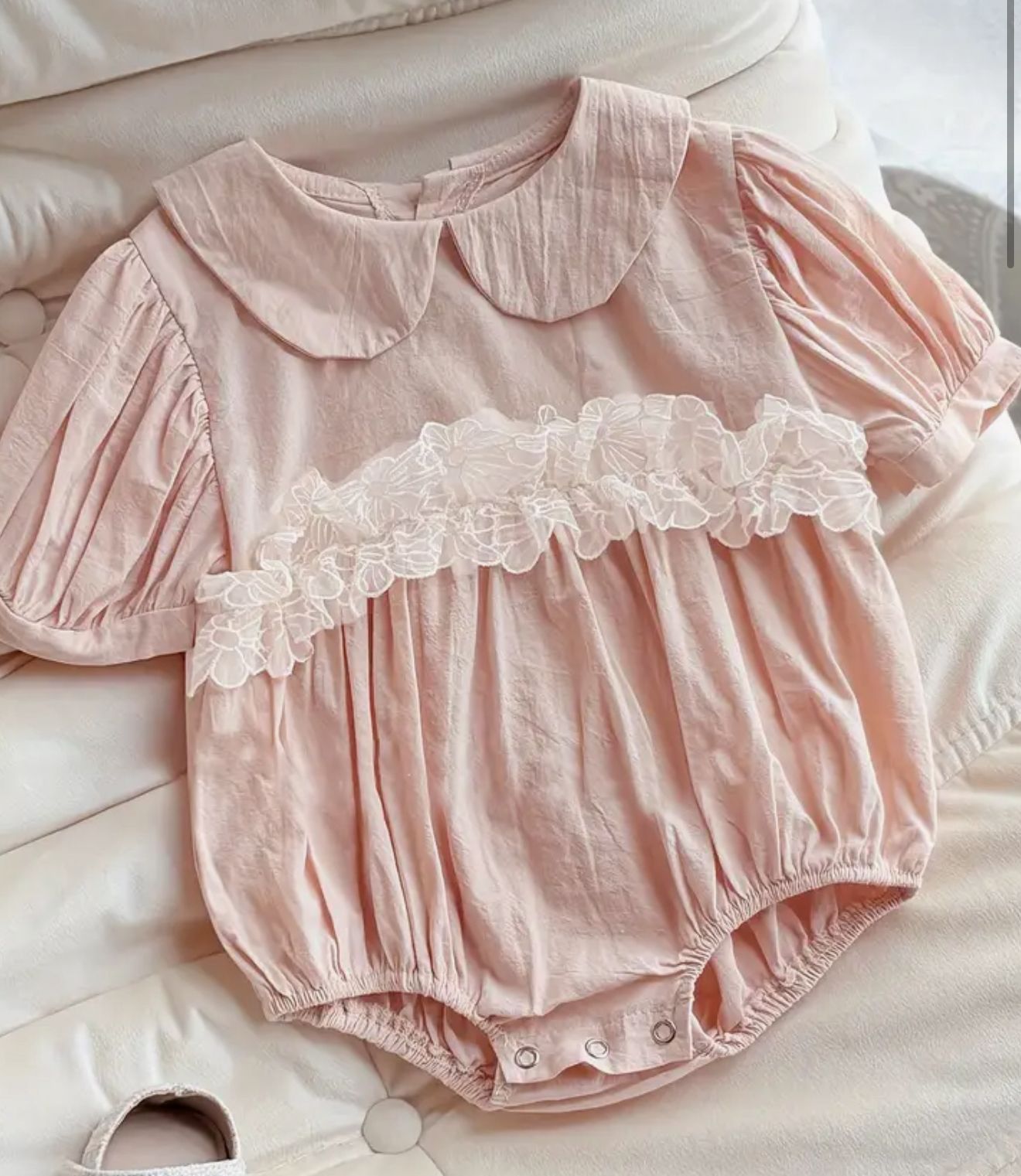 Pink baby romper with lace details on a light background