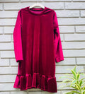 Red dress with long sleeves and ruffled hem on a hanger against a brick wall.