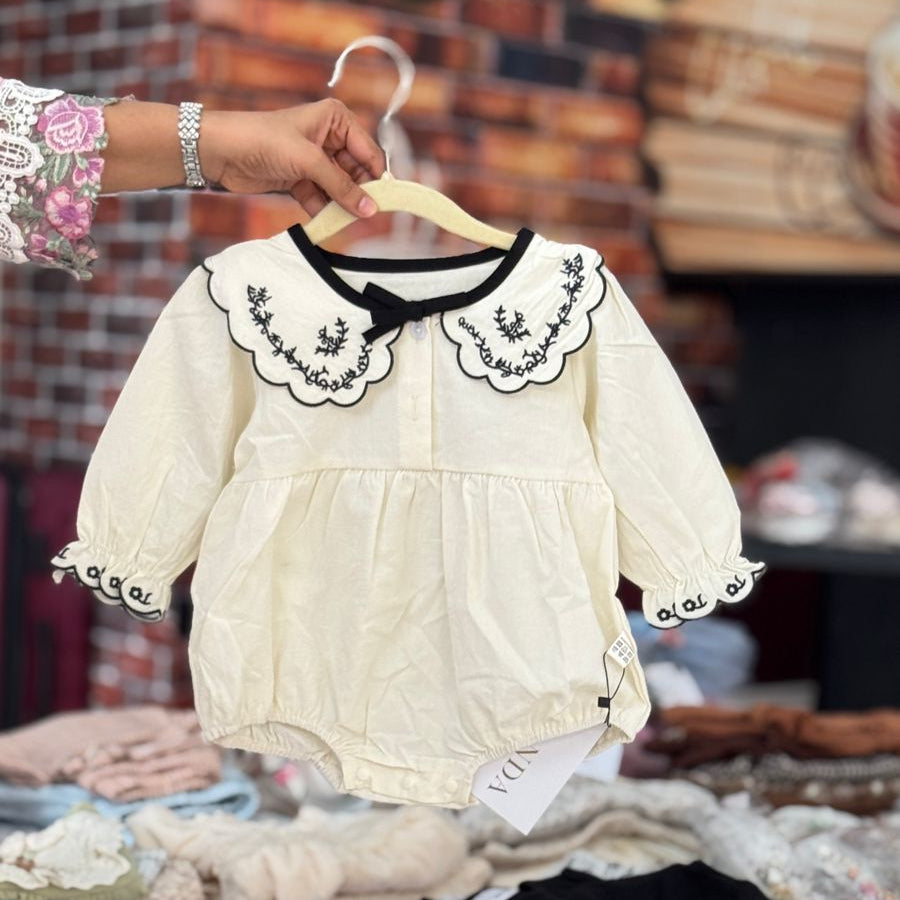 A vintage collar romper in cream and black, displayed on a hanger among other clothing items.