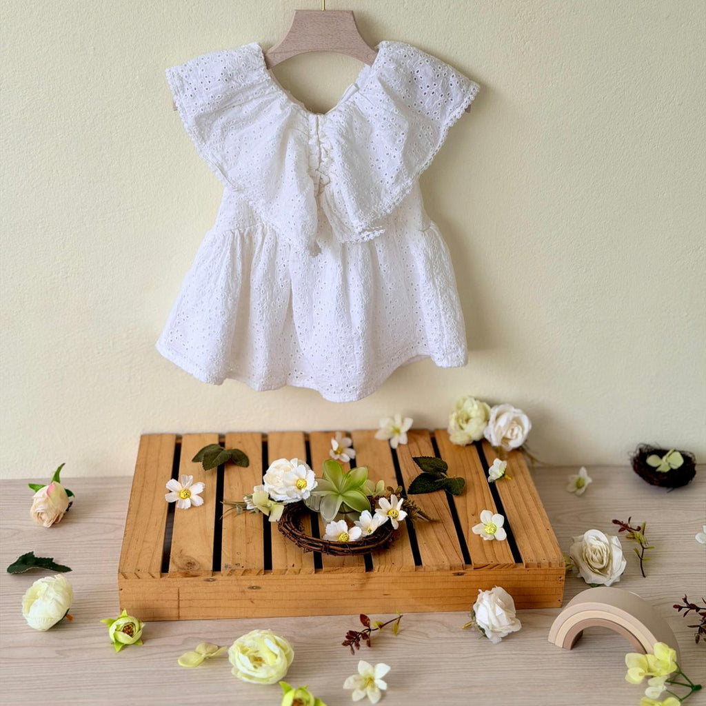White lace top on a wooden hanger with a wooden tray and decorative flowers on a light background