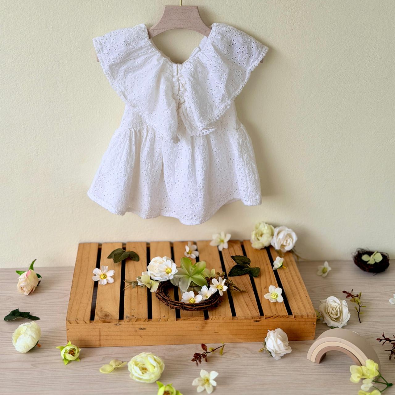 White lace top on a wooden hanger with a wooden tray and decorative flowers on a light background