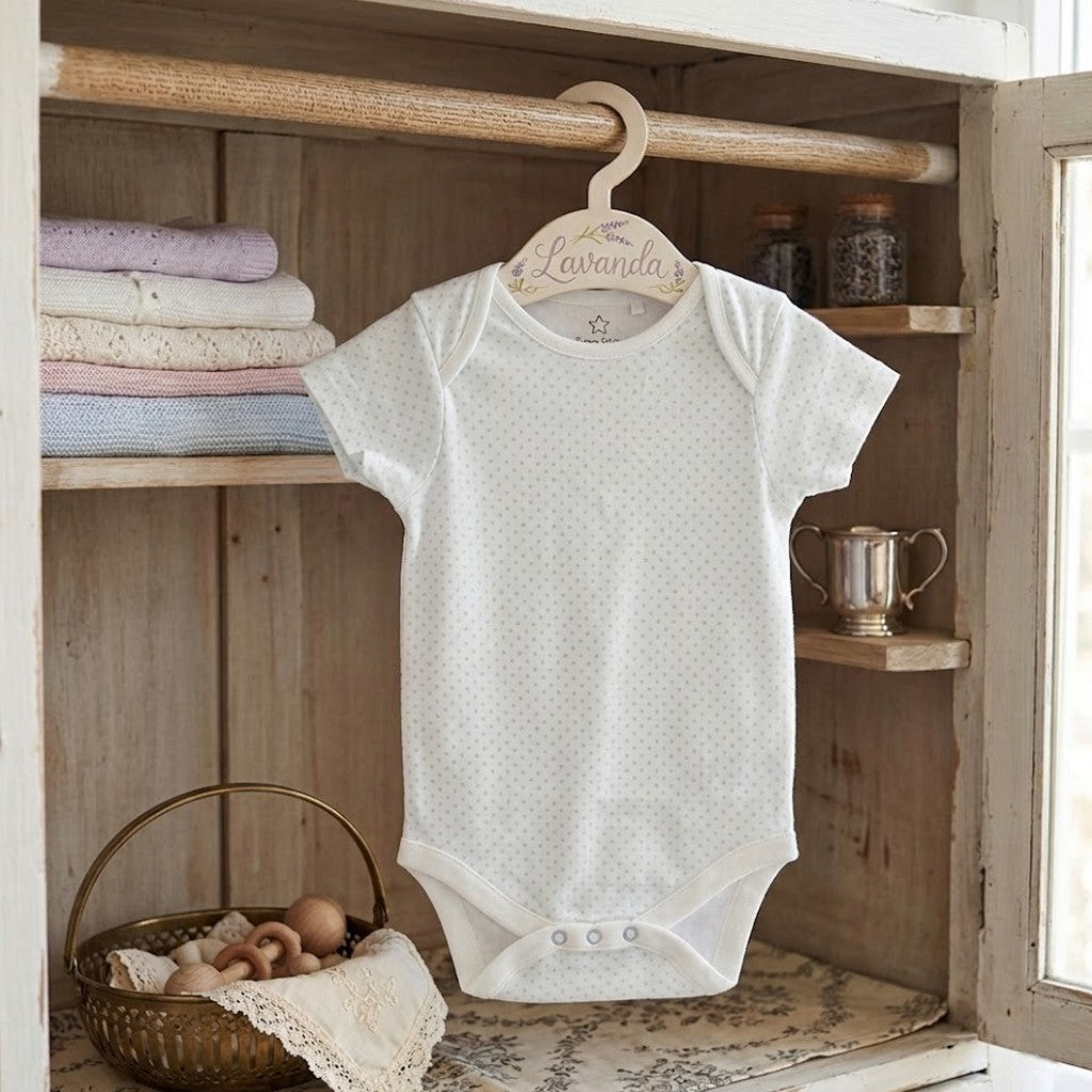 White baby onesie on a hanger with 'Lavender' label in a rustic wooden setting.