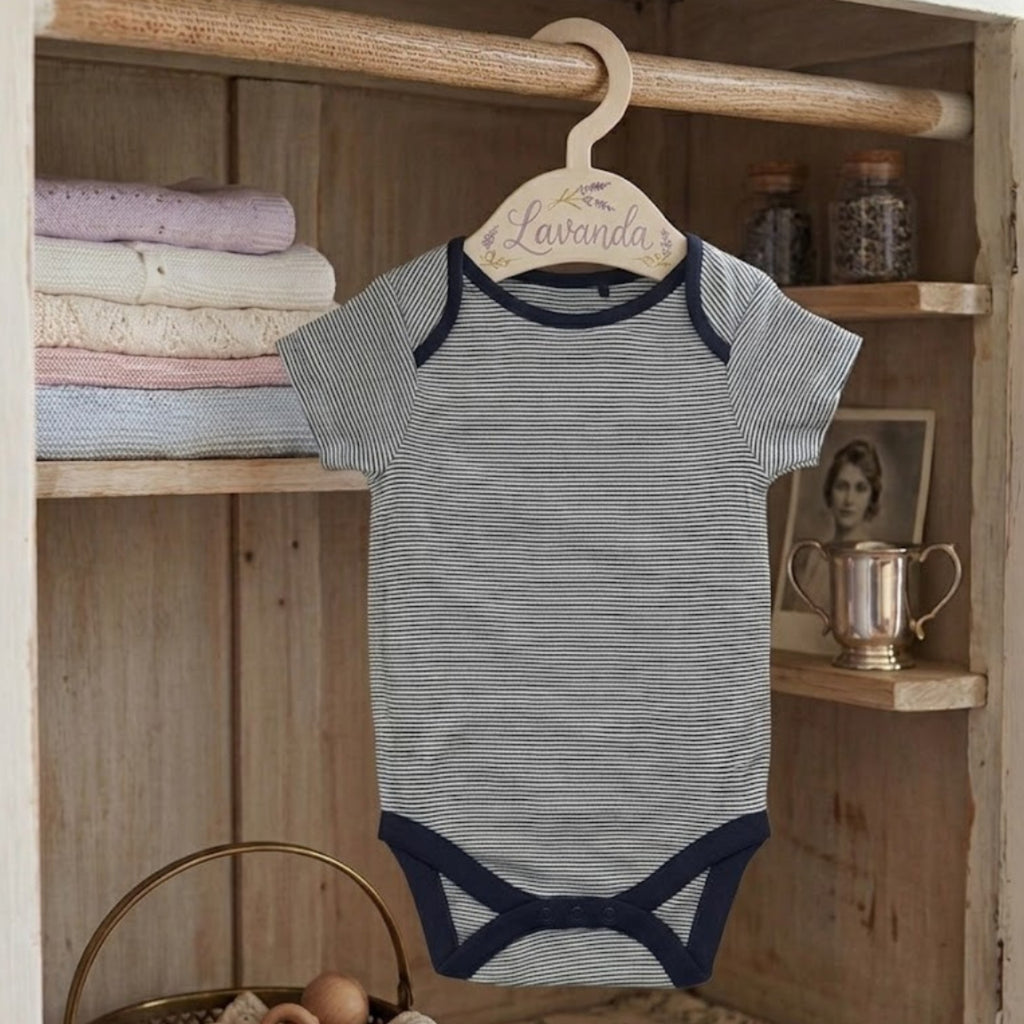 Striped baby onesie on a hanger with a wooden shelf in the background