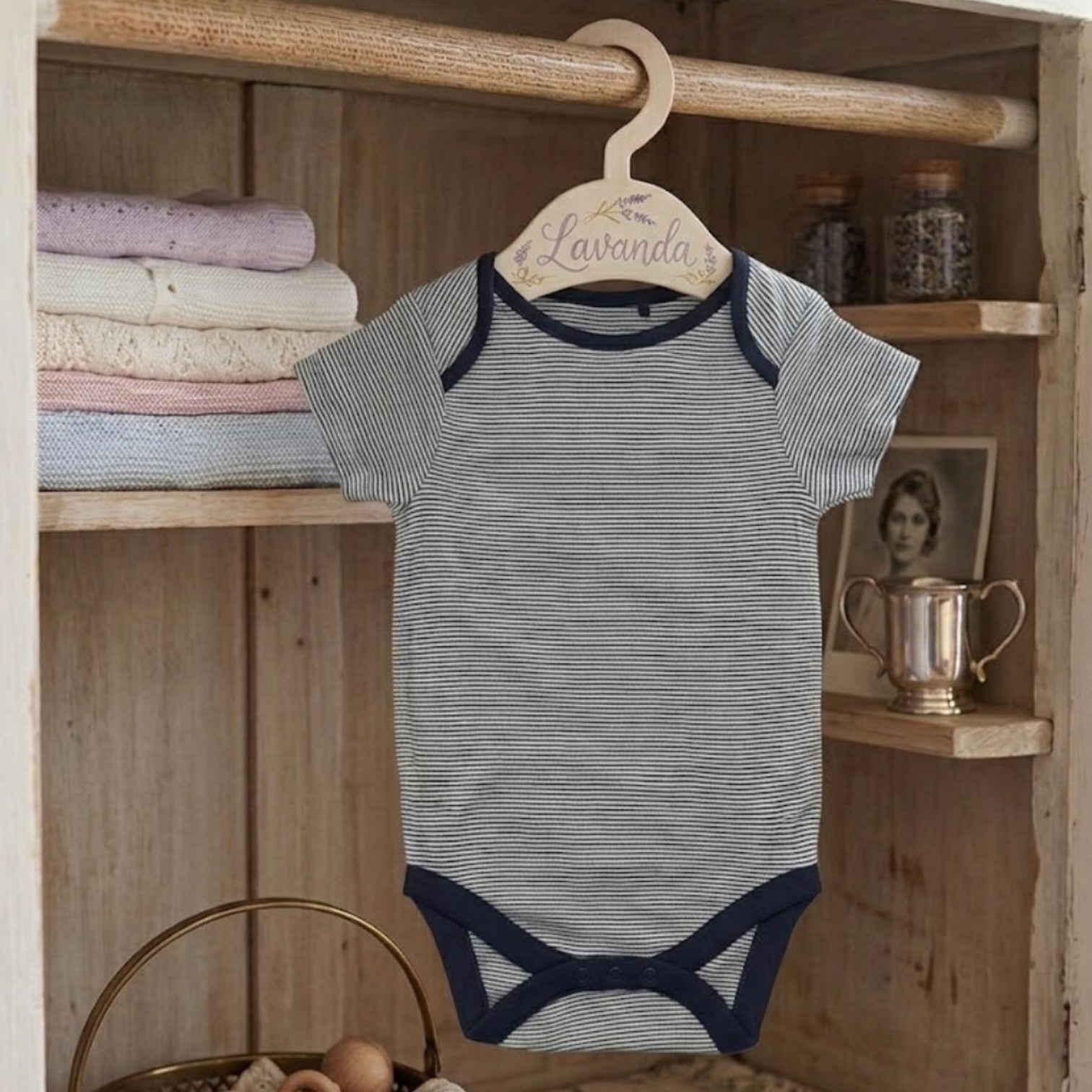 Striped baby onesie on a hanger with a wooden shelf in the background