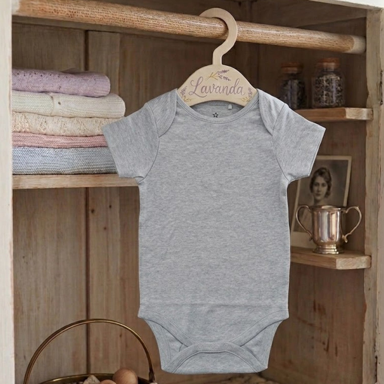 Gray baby onesie on a wooden hanger against a wooden shelf background